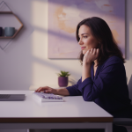 Mulher empreendedora sorrindo com confiança em frente ao seu laptop em um home office minimalista com tons de roxo e cinza. A imagem representa o sucesso e a tranquilidade de quem utiliza as tecnologias certas para escalar vendas no e-commerce.